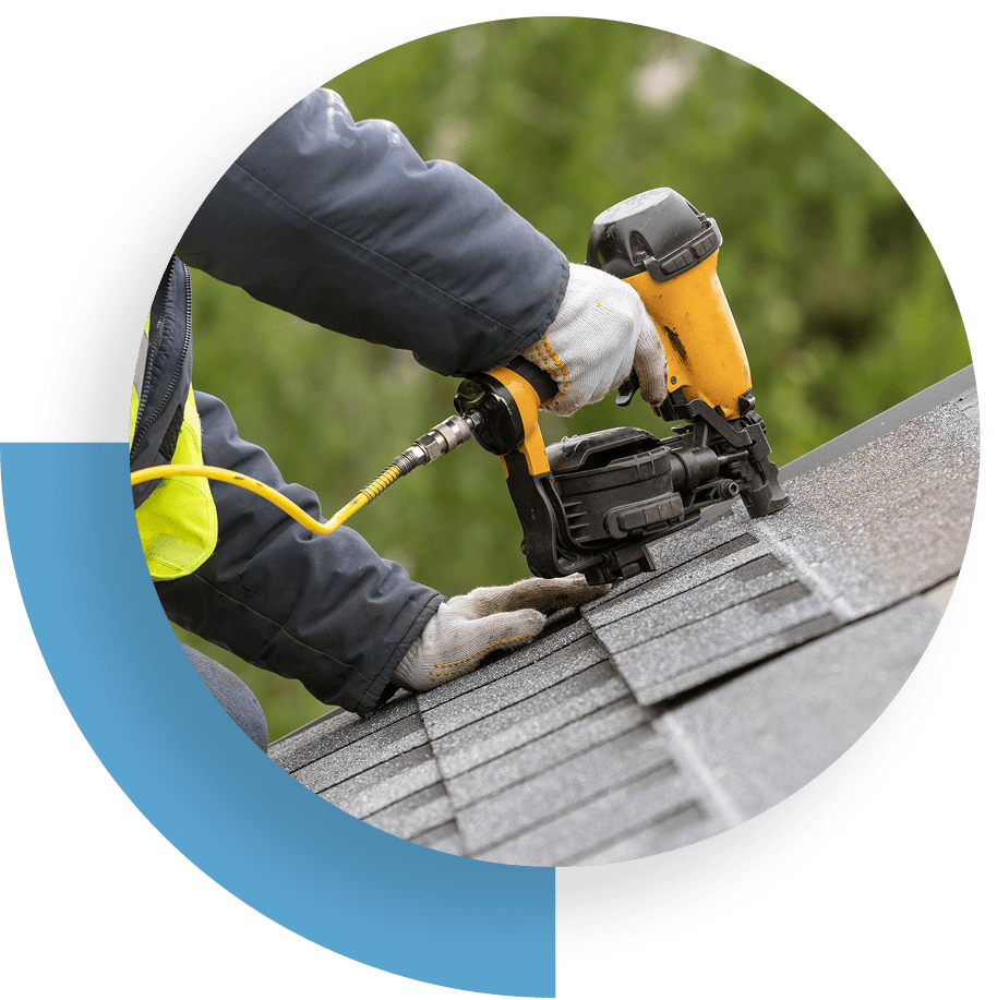 Worker installing black roof tiles with tools and gloves.