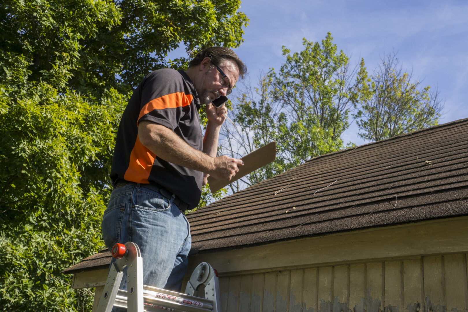 Man on ladder using a power drill on a roof edge.
