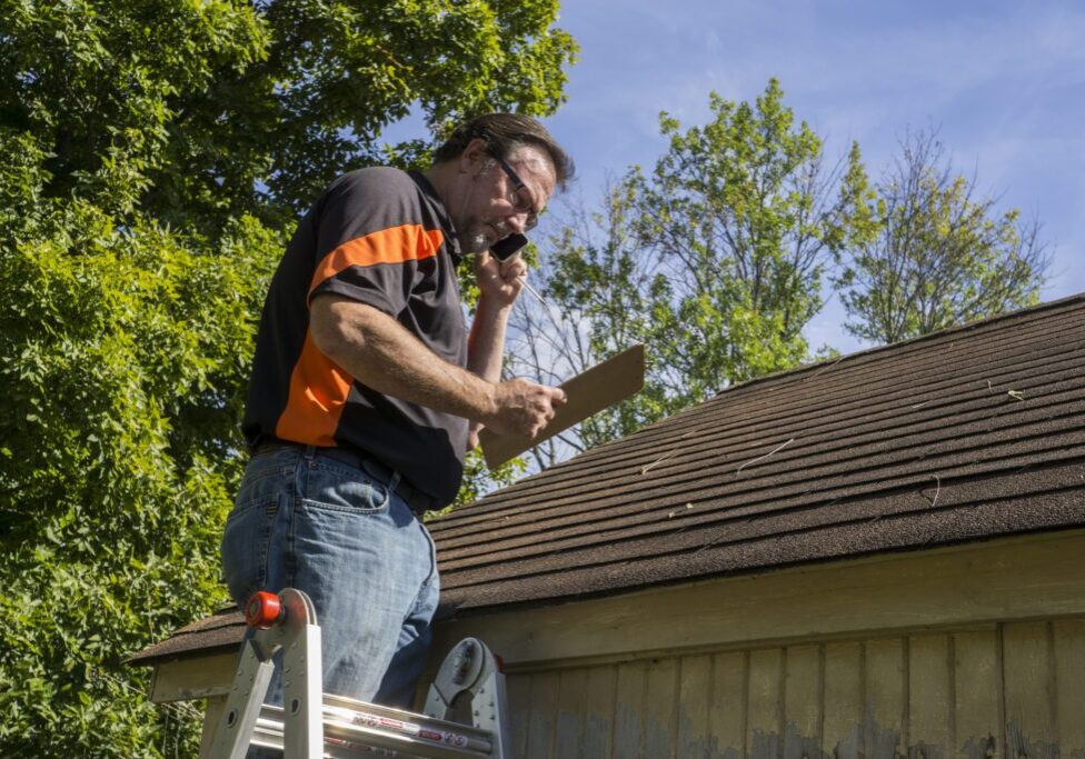 Man on ladder using a power drill on a roof edge.